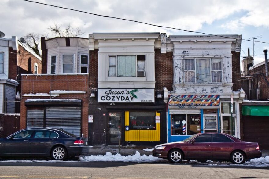 Small neighborhood storefronts with cars parked outside.